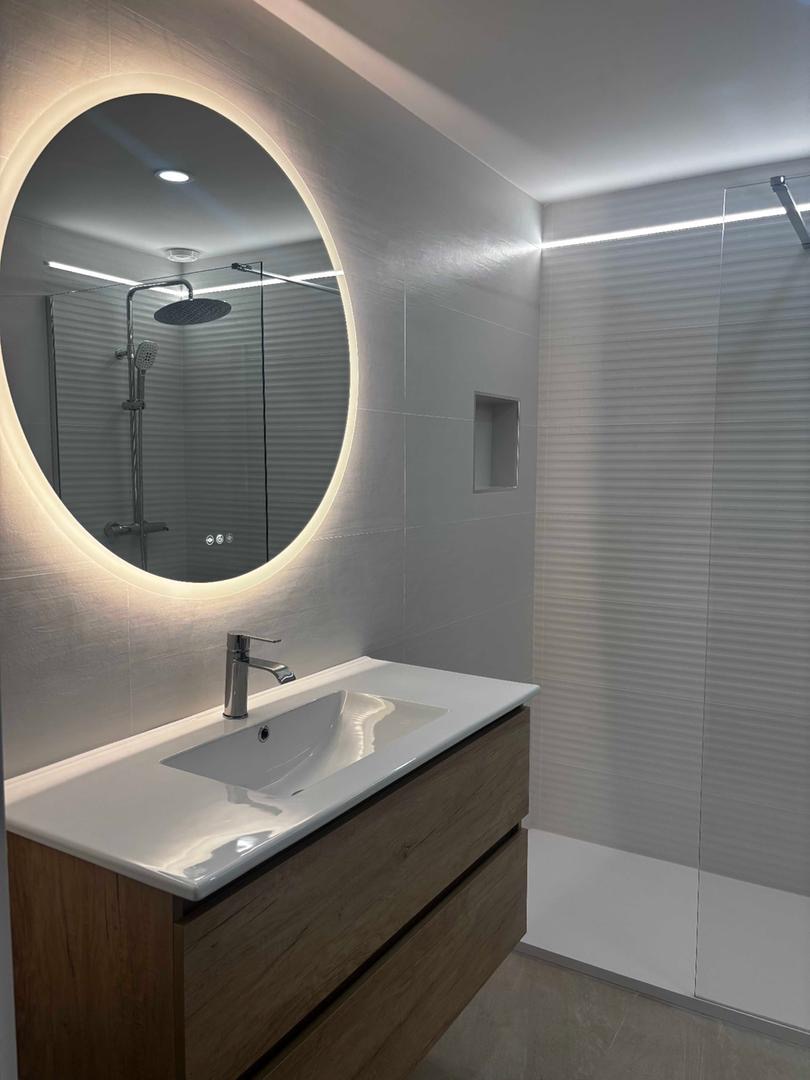 Baño moderno con espejo redondo LED retroiluminado y mueble suspendido de madera