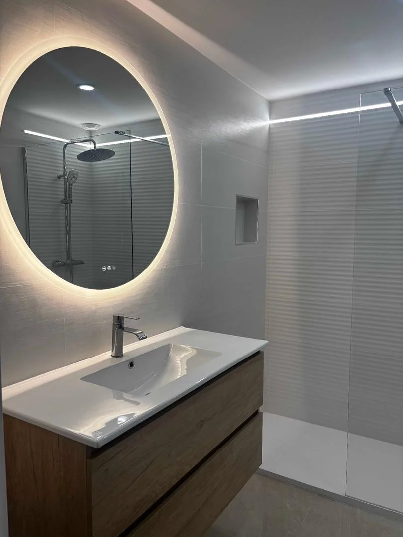 Baño moderno con espejo redondo LED retroiluminado y mueble suspendido de madera