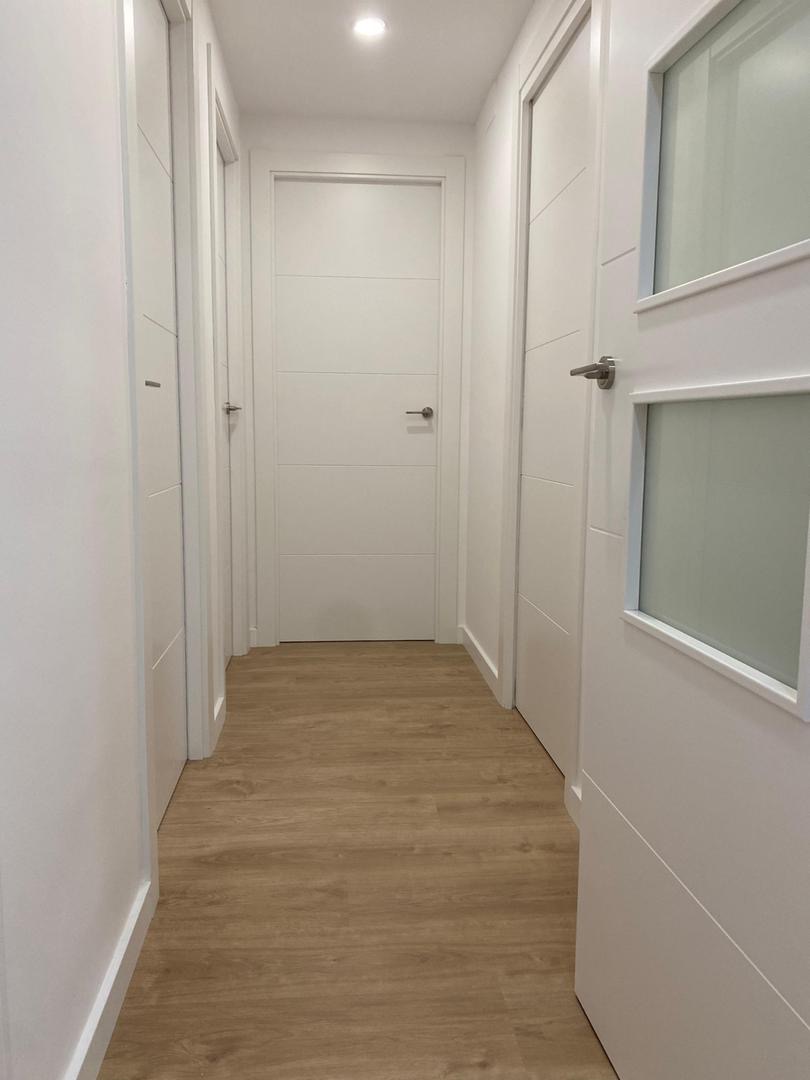 Pasillo reformado con puertas lacadas blancas y suelo de madera natural