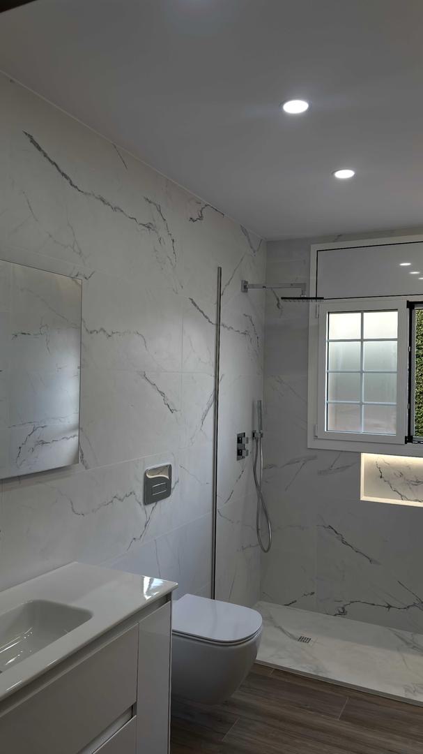 Baño con revestimiento de mármol blanco, ducha a ras de suelo y hornacina iluminada
