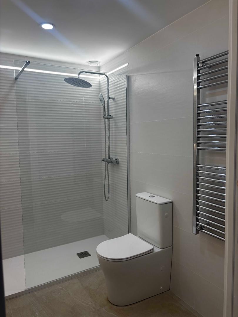 Baño con ducha de obra, columna de ducha cromada y toallero radiador
