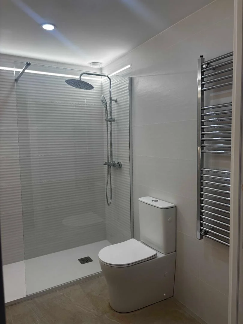 Baño con ducha de obra, columna de ducha cromada y toallero radiador