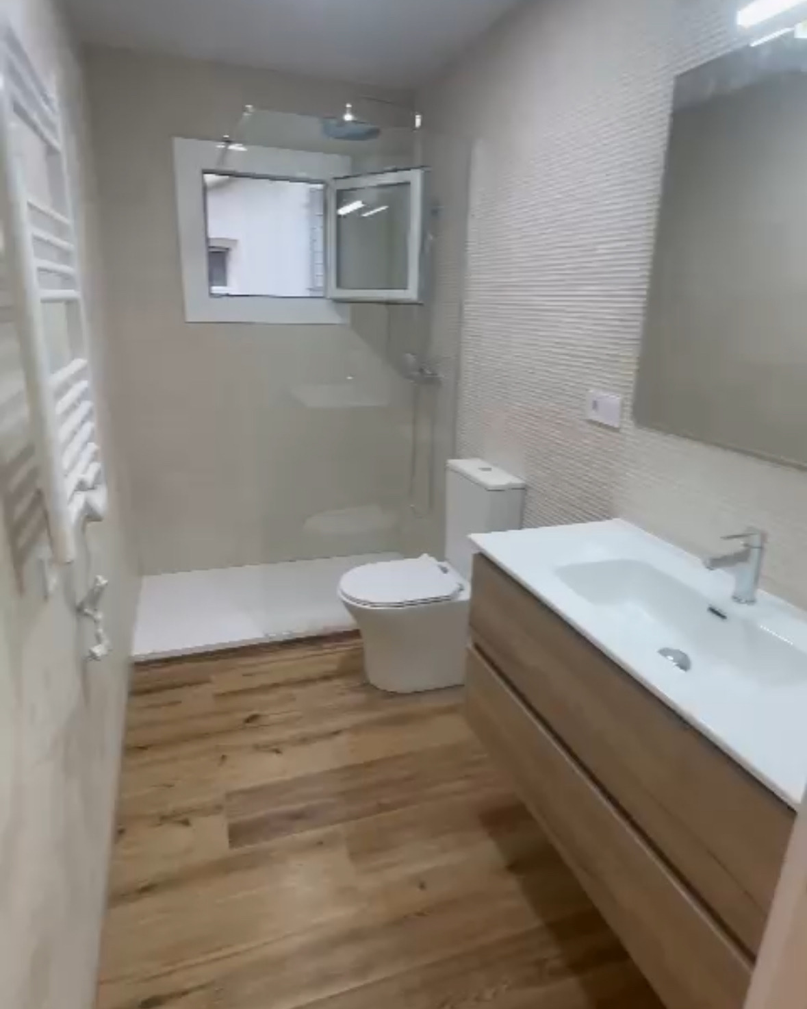 Baño con suelo de madera, mueble suspendido y azulejo texturizado