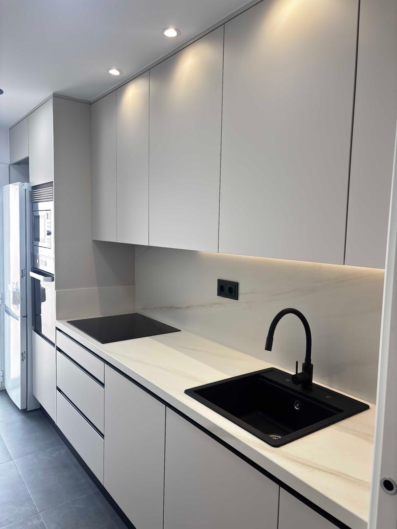 Cocina moderna con muebles blancos, encimera de mármol y grifo negro - Modela y Reforma