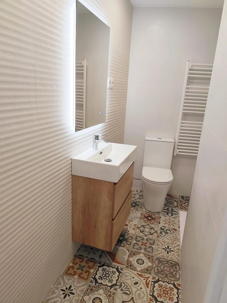 Reforma de aseo en Sabadell con suelo hidráulico, mueble de madera, espejo LED y azulejo blanco de relieve