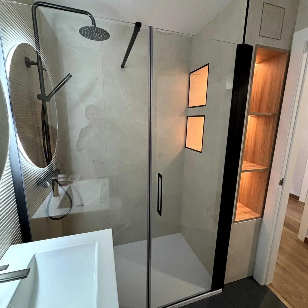 Ducha de obra con mampara, grifería negra mate, hornacinas iluminadas y estantería de madera a medida