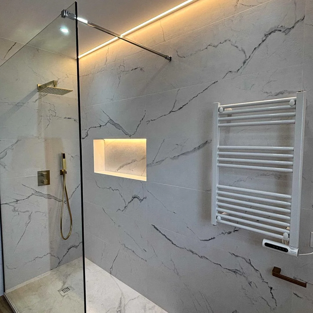 Ducha a ras de suelo con revestimiento de mármol, columna de ducha dorada y hornacina iluminada