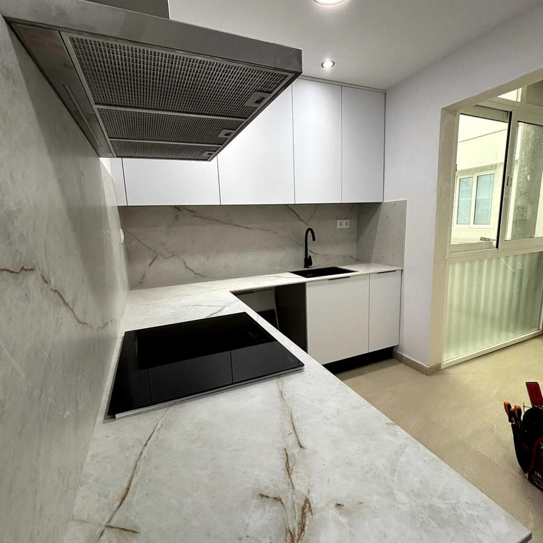 Reforma de cocina blanca en Sabadell con encimera de cuarcita, placa de inducción negra y campana de acero inoxidable