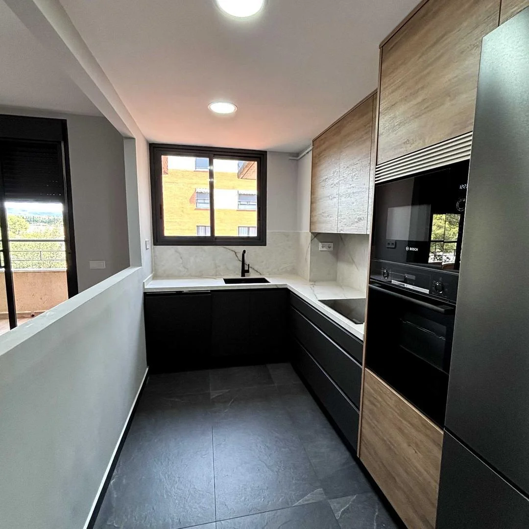 Reforma de cocina en U en Sabadell con muebles de madera y negro, encimera de mármol y suelo porcelánico gris