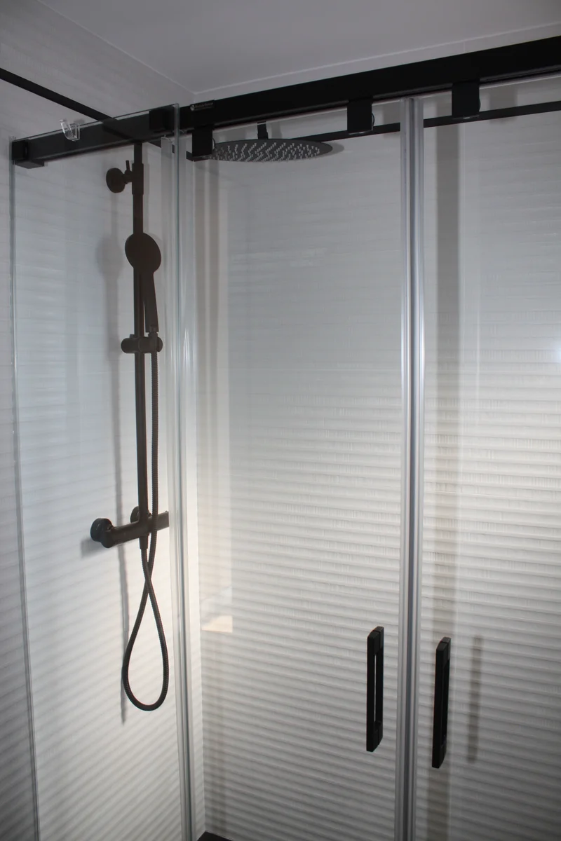 Baño reformado con columna de ducha negra mate y mampara corredera de cristal