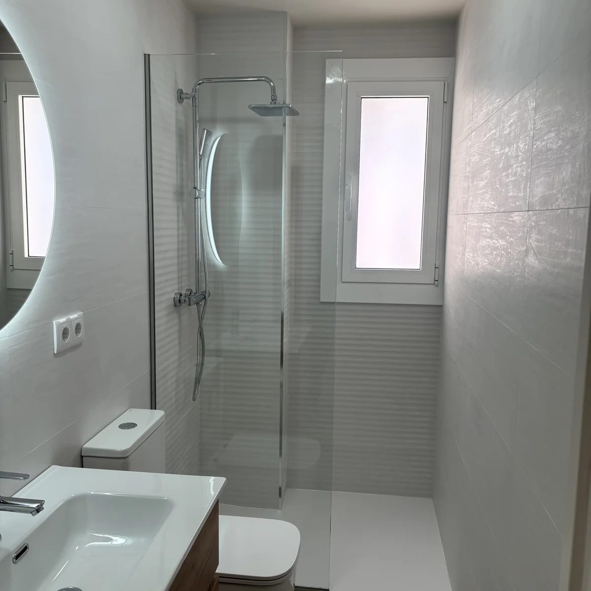 Reforma de baño en Sabadell en blanco con plato de ducha a ras de suelo, mampara y espejo LED redondo