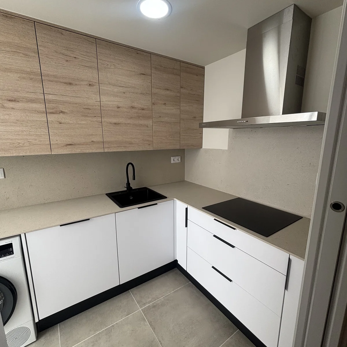Reforma de cocina en L con muebles de madera y blanco, encimera clara y fregadero negro