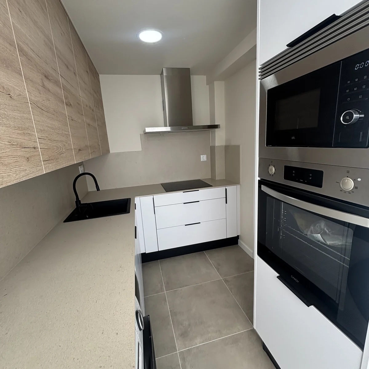 Cocina reformada con horno y microondas integrados, fregadero negro y campana de acero